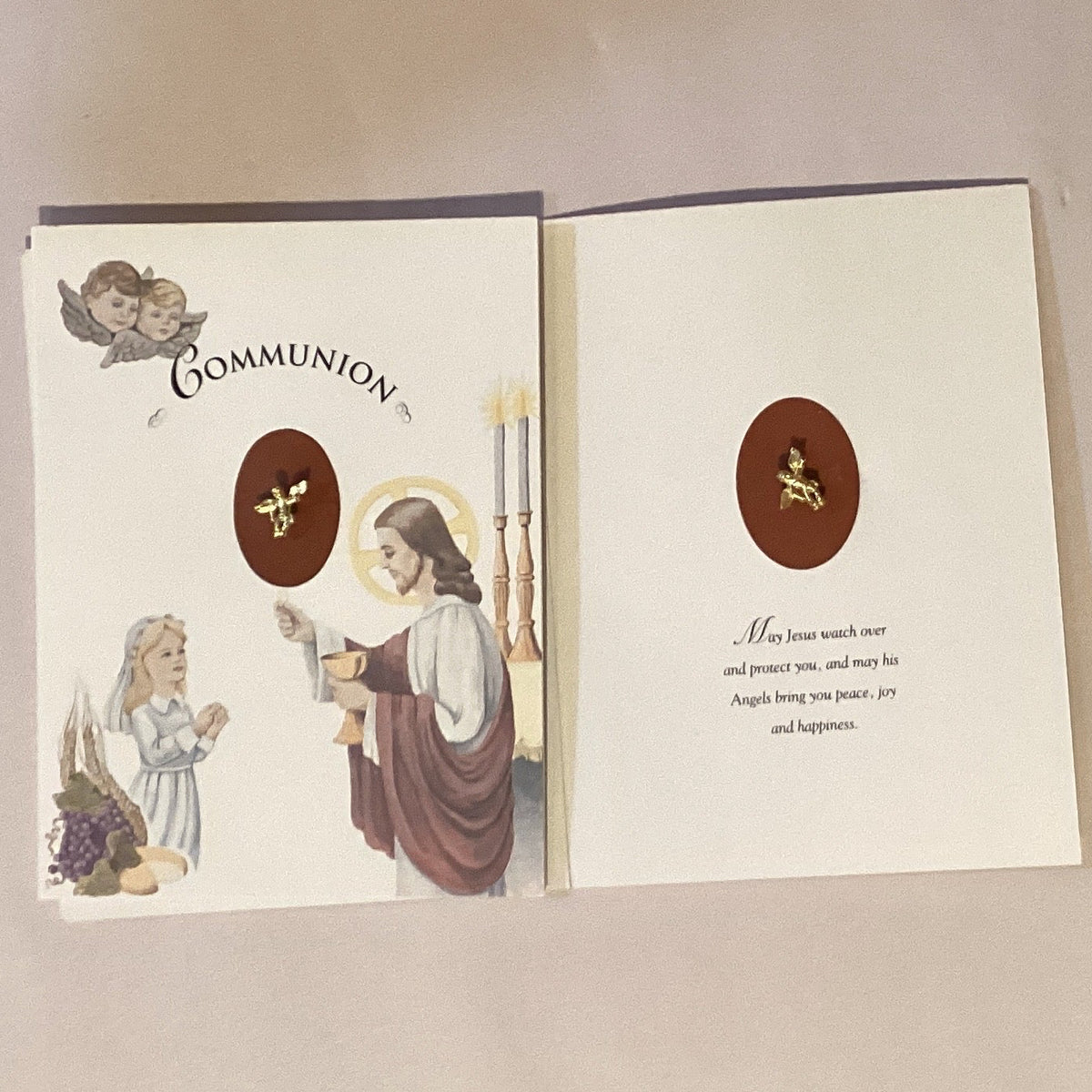 First Communion Catholic card featuring an angel keepsake pin, with religious imagery and Christian greeting details.