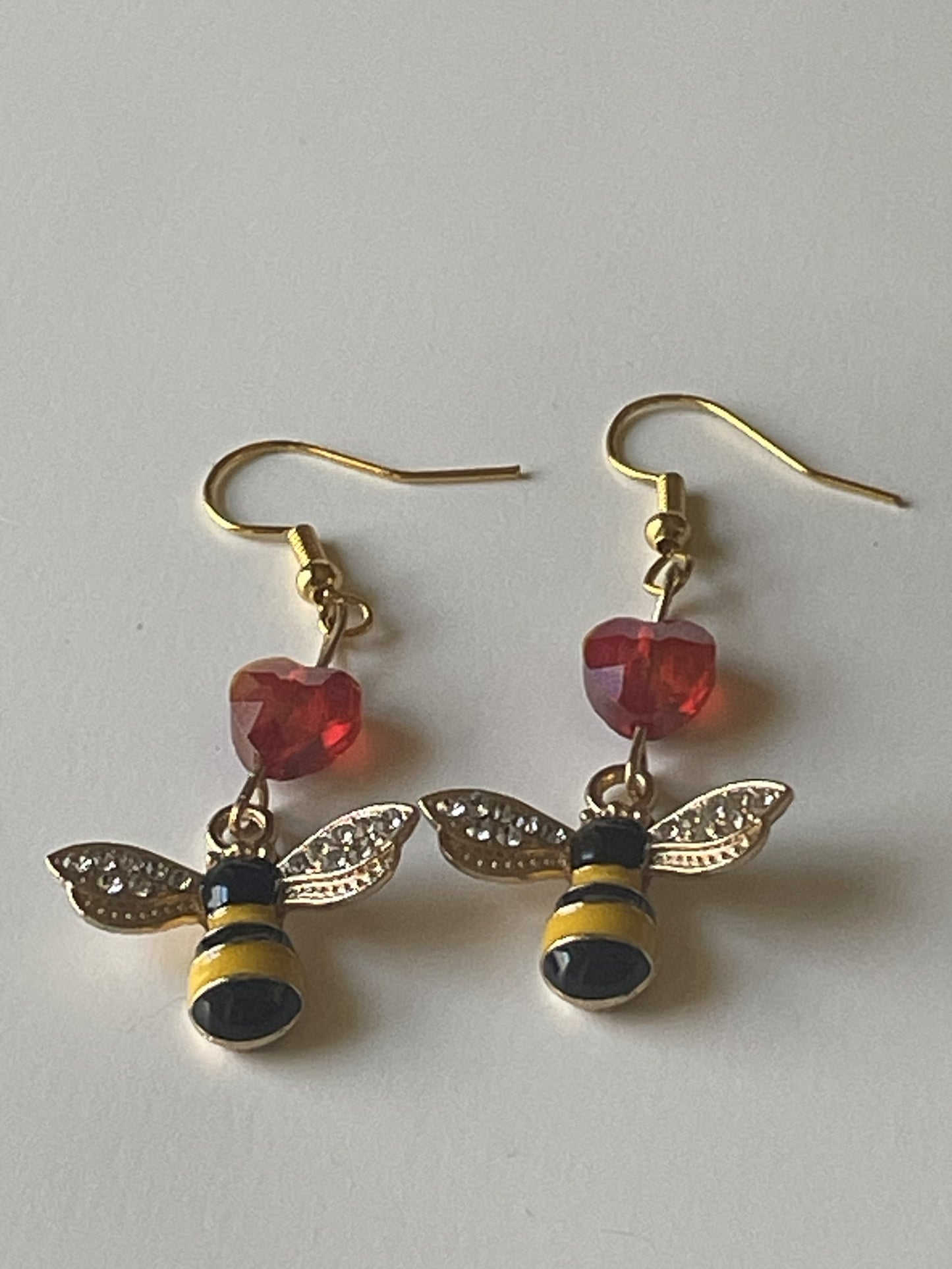 Gold-trimmed bee charm dangle earrings by Sylvia Leroux featuring sparkly bead accents and red acrylic heart beads on gold hooks.
