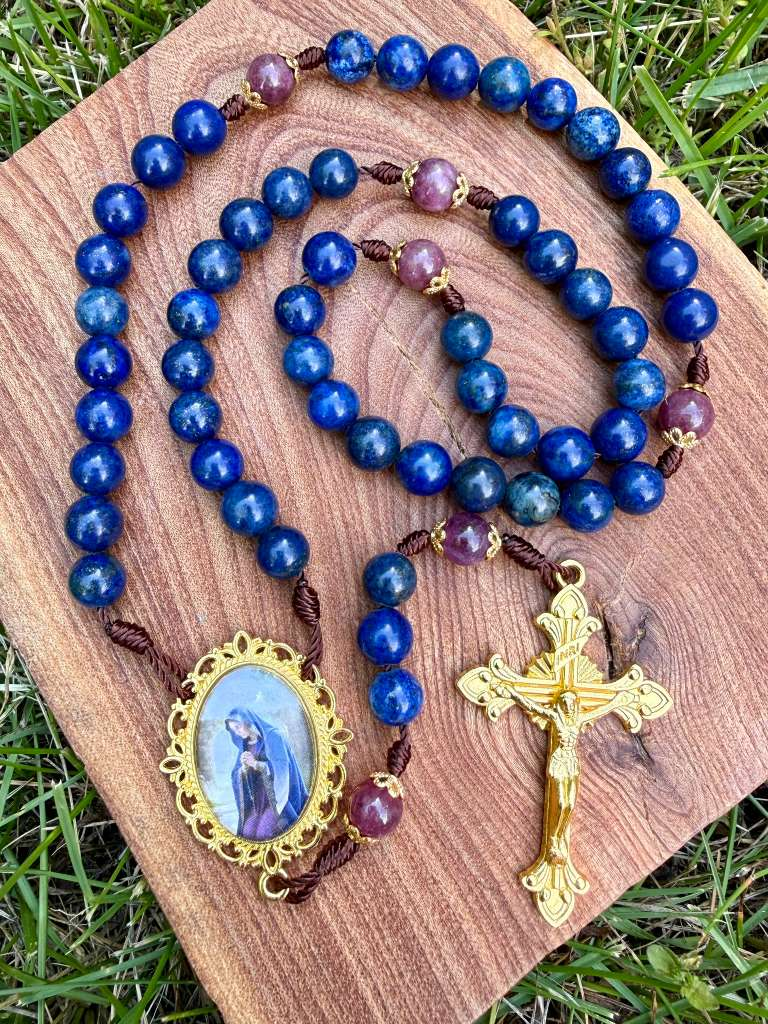 Ornate gold-toned Catholic rosary with Lapis Lazuli and purple quartz beads, featuring a praying Mary centerpiece and crucifix.