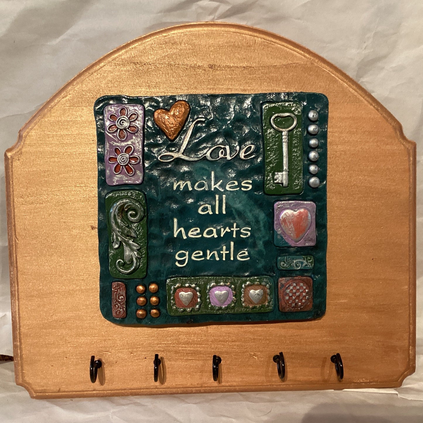Decorative 10-inch plaque with hooks featuring "Love makes all hearts gentle" phrase, crafted by Ysleta Mission Gift Shop.