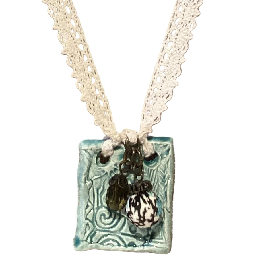 Turquoise embossed clay pendant necklace with cream lace and metal accents, 6.5 inches, handmade jewelry by Ysleta Mission Gift Shop.