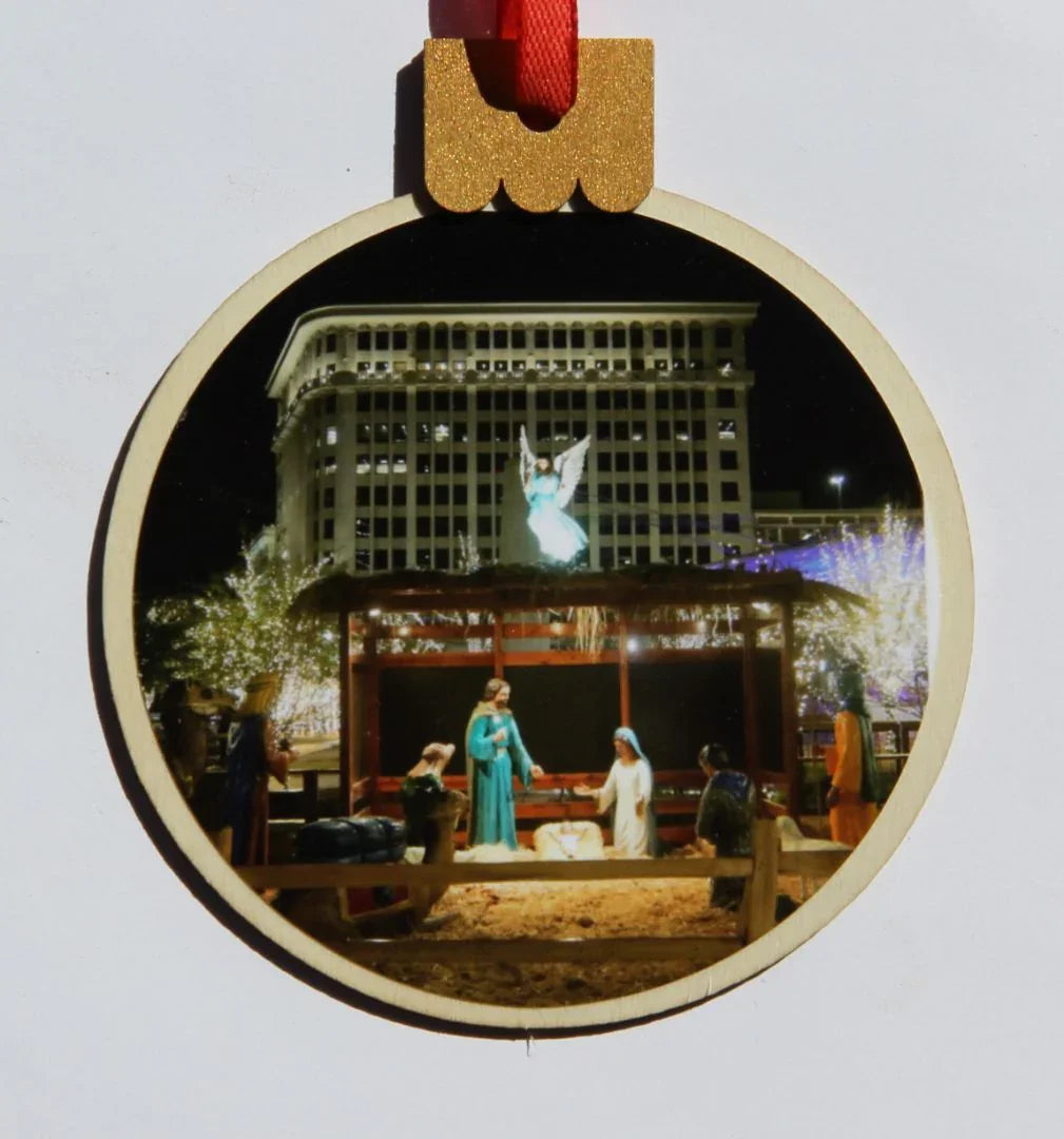 Wood round Christmas ornament featuring a downtown nativity scene, by Miguel Martinez, measures 3.77 x 4.29 inches.