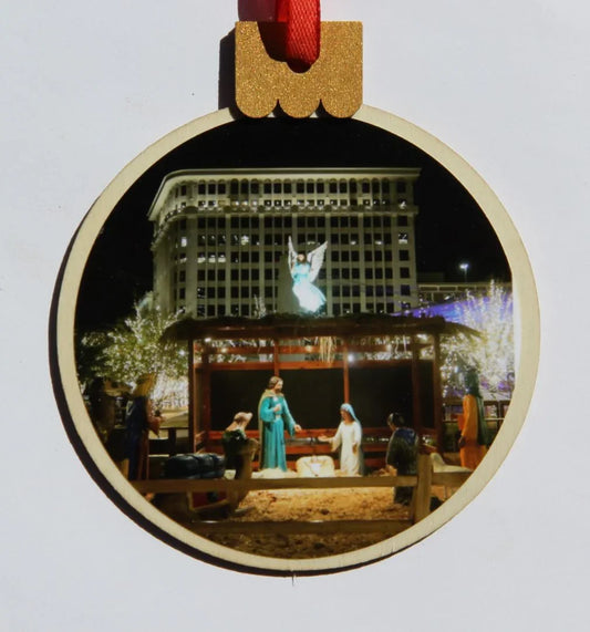 Wood round Christmas ornament featuring a downtown nativity scene, by Miguel Martinez, measures 3.77 x 4.29 inches.